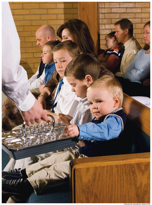 A photo of a young man passing the sacrament to a young family at a Mormon church.