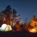 A lighted tent by a campfire.