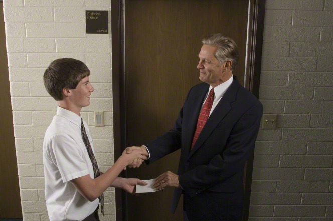A young man pays his tithing to the bishop of his ward.